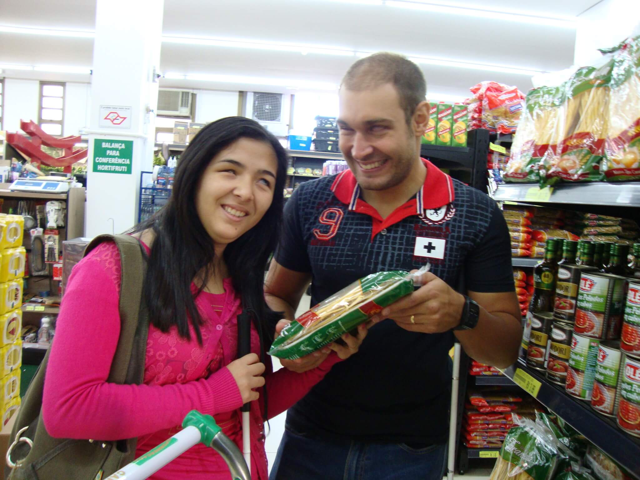 Um casal de adultos deficientes visuais fazendo compras no supermercado.